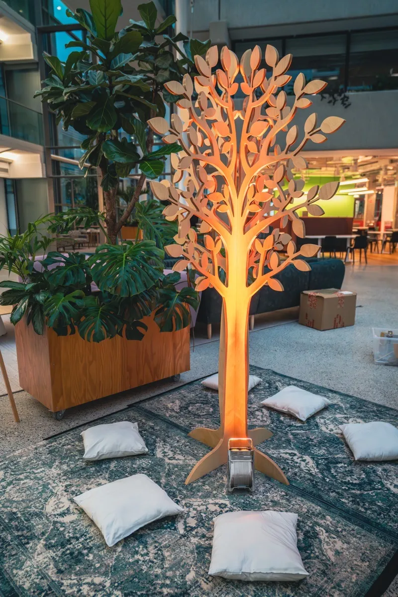 Illuminated wooden tree installation with cushions at Meta offices